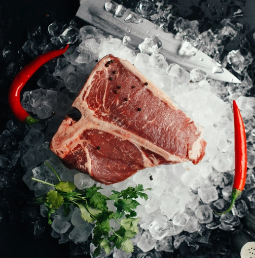 Côte de bœuf crue sur glace avec piment et herbes fraîches